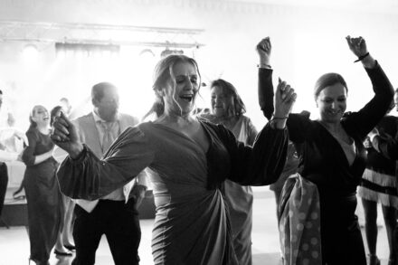 Two guests dance with their arms in the air on the dance floor during the party, in black and white
