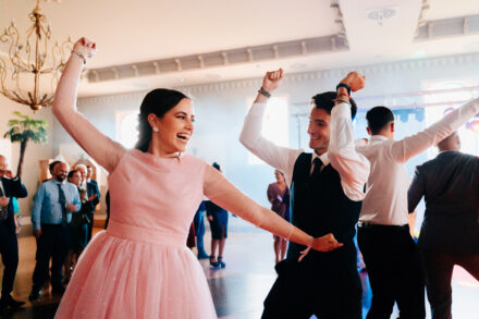 A guest in a pink dress and a guest in a waistcoat dance with raised fists on the dance floor