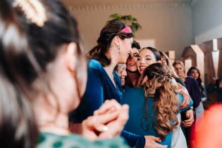 The bride gets a laughing group hug in the middle of a circle of guests