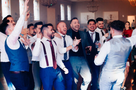 A group of guests laugh with their arms up facing the groom, seen from behind, at Hacienda Al-Baraka (Seville)