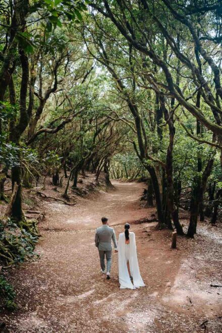 Los novios caminan de la mano, de espaldas, por un sendero bajo los árboles del parque rural de Anaga