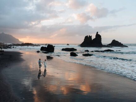 Vista aérea de los novios paseando por la orilla de la playa de Benijo, de arena negra, al atardecer