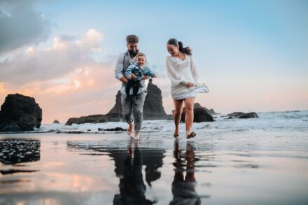 Los novios corren descalzos por la orilla, él con un bebé en brazos, en la playa de Benijo al atardecer