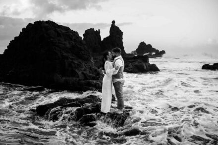 Los novios se besan sobre una roca rodeada de la espuma de las olas, en blanco y negro