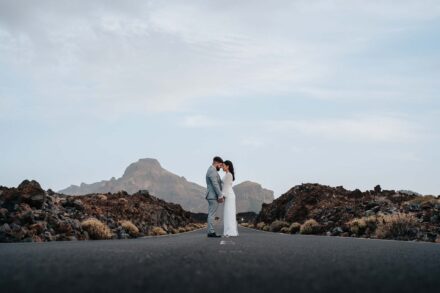 Los novios frente con frente en mitad de una carretera vacía entre coladas de lava, con una montaña rocosa al fondo