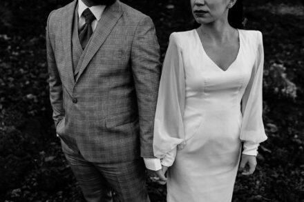 Detalle de los novios de la mano, él con traje de cuadros y ella con vestido de mangas abullonadas, en blanco y negro