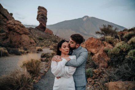 El novio abraza por detrás a la novia, que cierra los ojos mientras él le besa la sien, con el Teide al fondo
