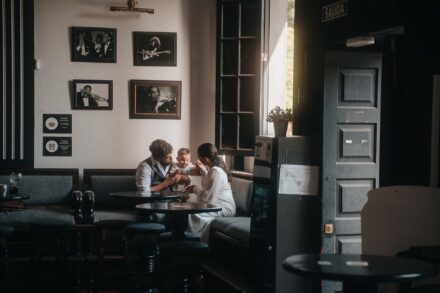 Los novios juegan con un bebé sentados a la mesa del bar, junto a una ventana por la que entra la luz