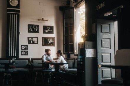 Los novios charlan sentados a una mesa de un bar con fotos de músicos en la pared, junto a una ventana
