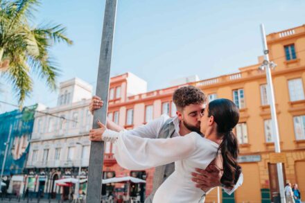 Los novios se besan agarrados a un poste, entre edificios de colores y una palmera