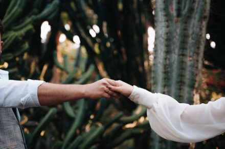 Los novios se dan la mano con los brazos estirados ante unos cactus gigantes, en su postboda en Tenerife