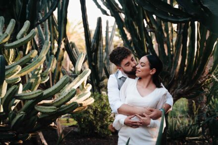 El novio abraza por detrás a la novia y le besa la mejilla entre cactus altos