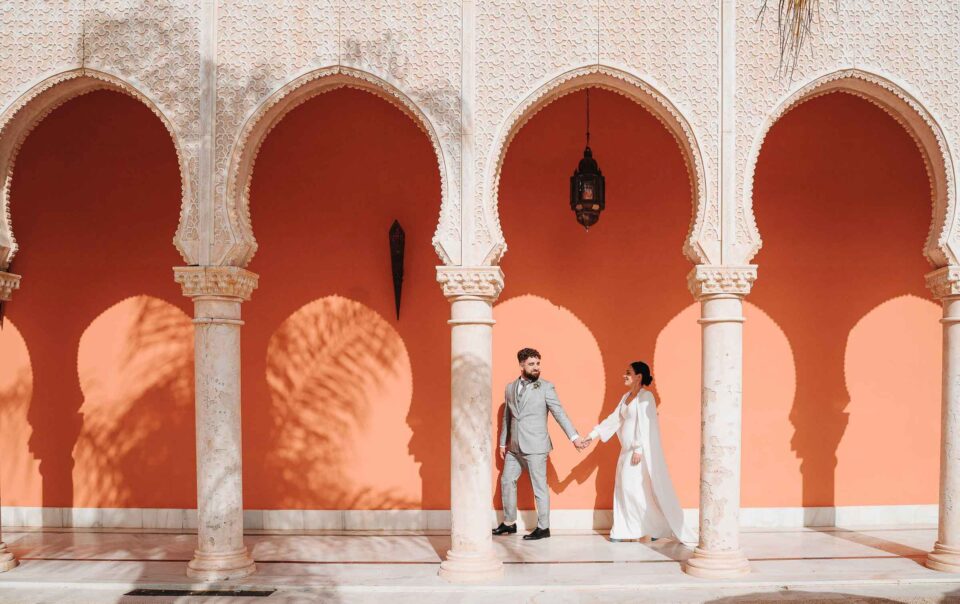 Bride and groom walking hand in hand through Moorish arches during a destination wedding in Seville, Spain