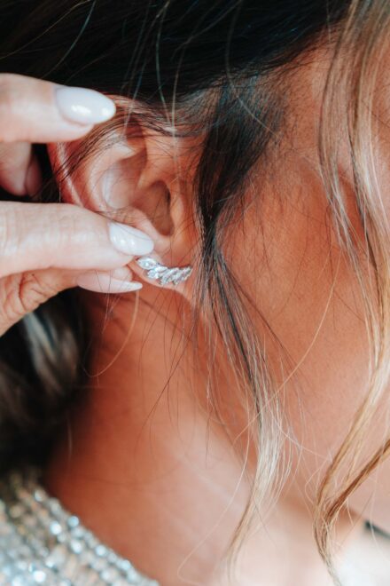 Una mano ajusta en la oreja de la novia un pendiente de brillantes en forma de ramita, de cerca