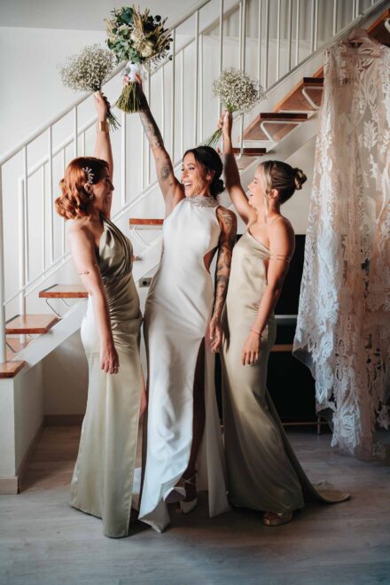 La novia, Andrea Medina y otra amiga, de satén verde, levantan sus ramos al pie de la escalera