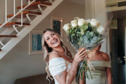 La novia ríe a carcajadas sosteniendo un gran ramo de rosas blancas envuelto en celofán