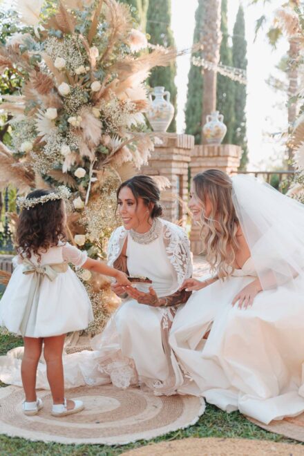 Una niña con corona de flores entrega una pequeña bandeja a las novias durante la ceremonia