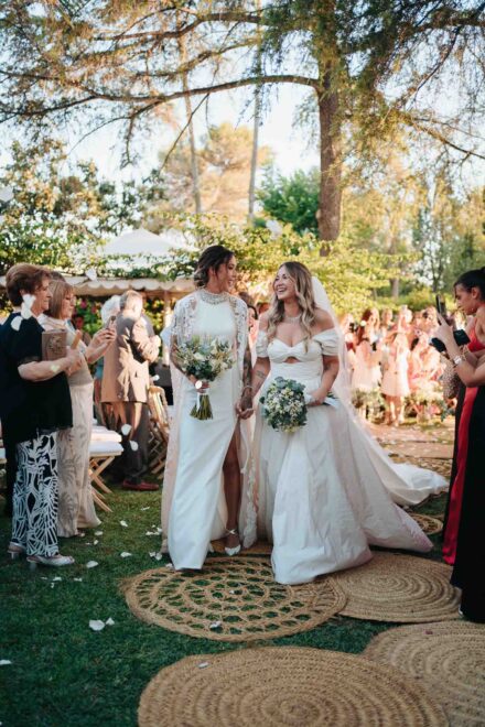 Las novias avanzan riendo mientras los invitados les lanzan pétalos al final del pasillo