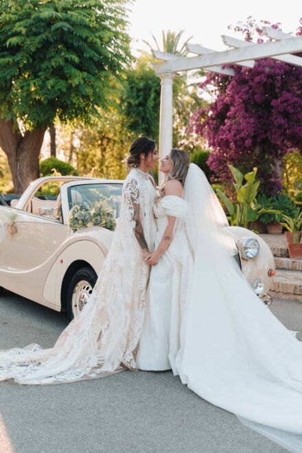 Las novias se miran de la mano junto al descapotable y la pérgola de buganvillas, en Finca Al-Yamanah (Sevilla)