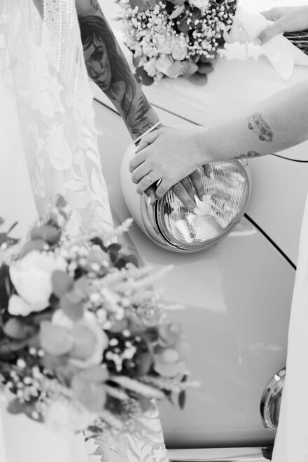 Las manos de las novias, una sobre otra, apoyadas en el faro del descapotable, en blanco y negro