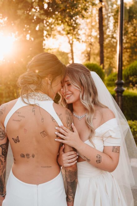Una de las novias, con la espalda al aire llena de pequeños tatuajes, junta la frente con la otra al atardecer
