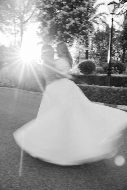 Las novias giran abrazadas a contraluz y la falda del vestido vuela, en blanco y negro