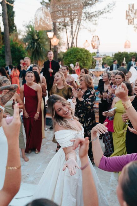 Una de las novias baila riendo con los ojos cerrados, rodeada de invitados que aplauden