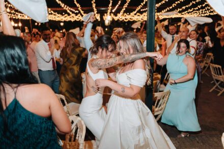 Las novias bailan abrazadas bajo las guirnaldas de luces mientras los invitados agitan servilletas
