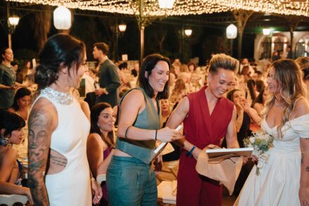 Dos invitadas sonrientes entregan a las novias regalos envueltos en papel marrón entre las mesas