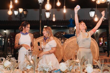 Una invitada celebra con los brazos en alto junto a las novias, que llevan pañuelos anudados al cuello