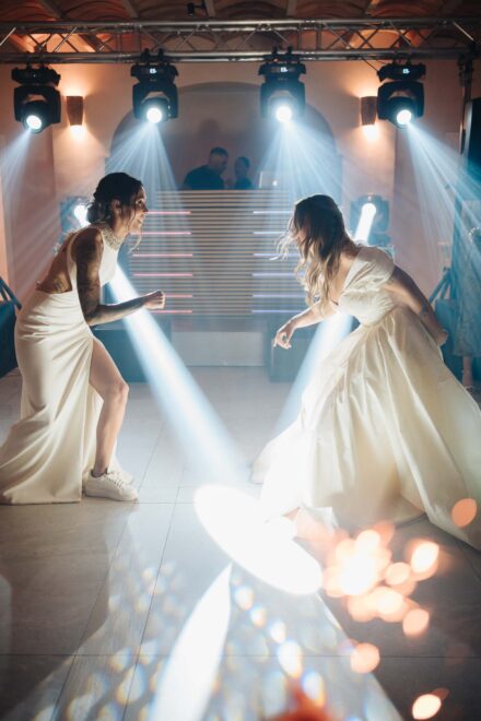 Las novias se agachan cara a cara en la pista de baile entre haces de luz