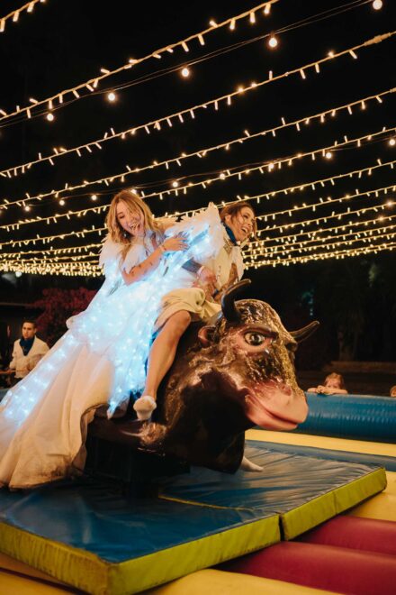 Las novias montan juntas en un toro mecánico, riendo bajo las guirnaldas de luces