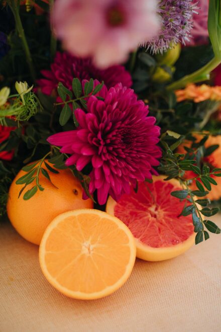 Detalle de un crisantemo fucsia junto a una naranja y un pomelo partidos por la mitad sobre el mantel