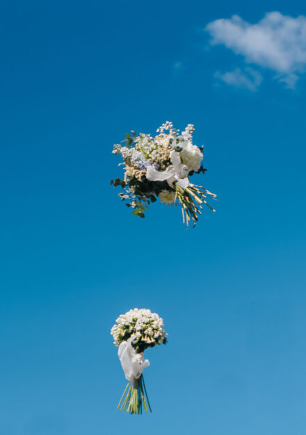 Dos ramos de flores blancas suspendidos en el aire contra un cielo azul con una nube