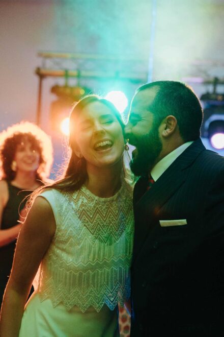 La novia, con top de lentejuelas en zigzag, se ríe a carcajadas con el novio pegado a su mejilla en la fiesta