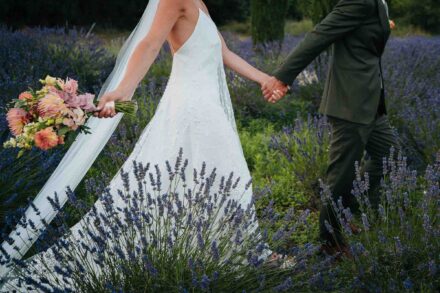 Los novios caminan de la mano entre matas de lavanda, sin que se les vea la cara; ella lleva el ramo y el velo