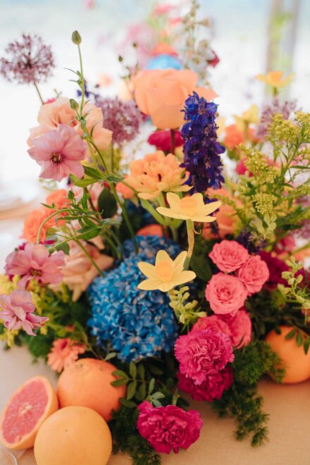Centro de mesa con hortensia azul, claveles fucsia, rosas melocotón y pomelos, uno partido por la mitad