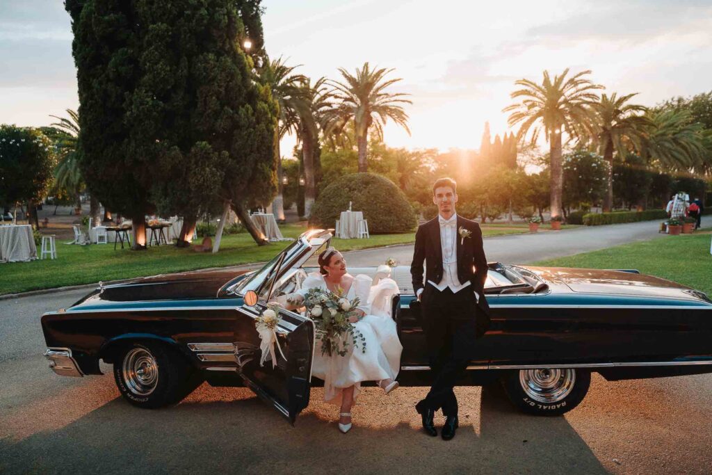 Bride and groom posing with a classic car under the Seville sunset