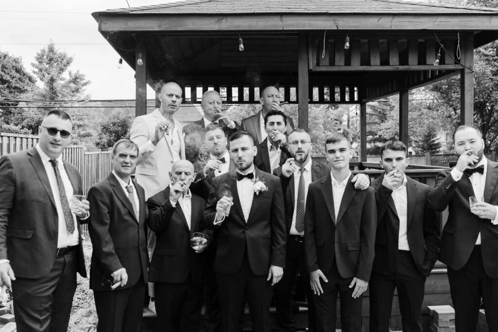 Black and white portrait of a group of men ?groom, family, and friends of Albanian and Italian roots? smoking cigars and sharing drinks in Toronto during a traditional Albanian wedding celebration