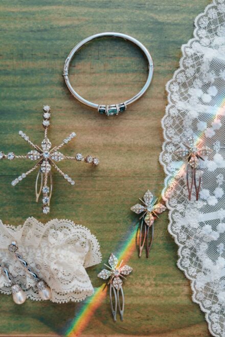 Pulsera, horquillas de pedrería, pendientes de perla y liga de encaje sobre madera, con un reflejo de arcoíris