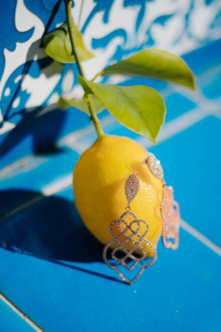 Pendientes de pedrería prendidos en un limón con hojas, sobre azulejos azules y blancos al sol