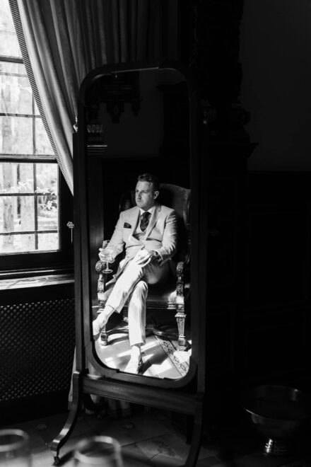 Groom portrait reflected in mirror holding a drink at Hacienda Villa Luisa wedding in Seville