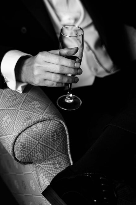 Black and white close-up of the groom holding a champagne glass during wedding preparations