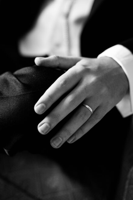 Black and white close-up of the groom’s hand with a wedding ring during wedding preparations.
