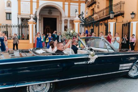 Bride arriving in a vintage convertible car outside a church in Seville with guests watching