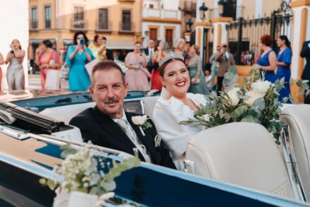 Bride arriving in a vintage convertible car outside a church in Seville with guests watching