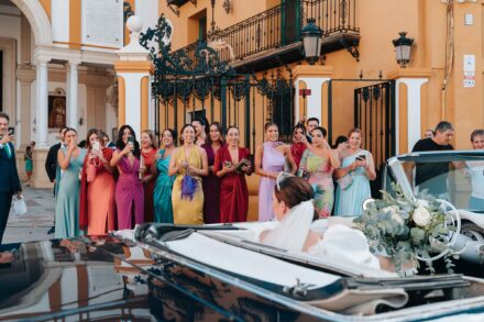 Bride arriving in a vintage convertible car outside a church in Seville with guests watching