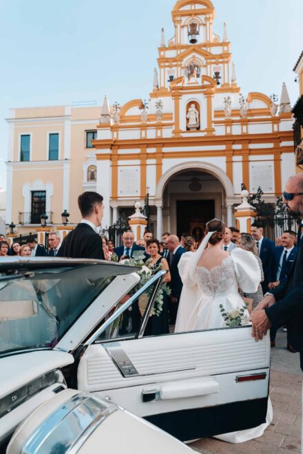 Bride and groom with guests outside Basilica de la Macarena in Seville next to a vintage wedding car