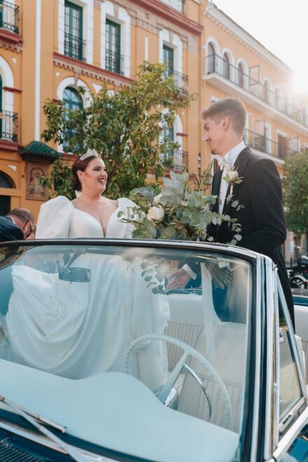 Bride and groom with guests outside Basilica de la Macarena in Seville next to a vintage wedding car