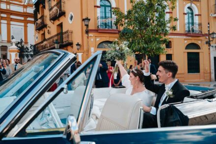Bride and groom with guests outside Basilica de la Macarena in Seville next to a vintage wedding car